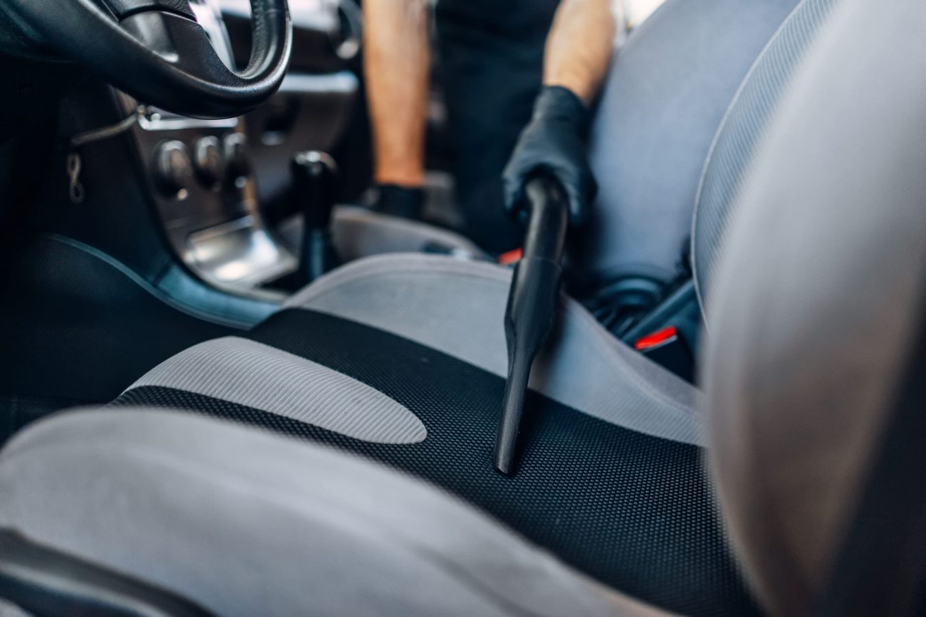 Auto detailing, cleaning seats with vacuum cleaner Auto detailing of car interior on carwash service. Worker in gloves cleaning seats with vacuum cleaner