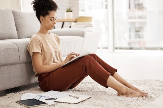 Freelance woman, laptop and typing email, communication or information for data analytics on carpet Freelance woman, laptop and typing email, communication or information for data analytics on carpet